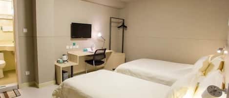 A hotel room with two beds, a desk, a chair, a TV, and a bathroom visible through an open door.