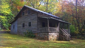 A rustic log cabin with a stone foundation, a porch, and a staircase leading to the entrance.