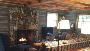 A cozy living room with a stone fireplace, a television, a sofa, a chair, and a lamp.