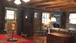 A rustic cabin interior with a wooden dining table, chairs, a sofa, and a chandelier.