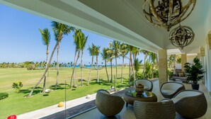 A spacious room with a view of a golf course and palm trees, furnished with modern chairs and a table. - Luxury Sunshine II. villa with SEA & GOLF VIEW, pool heated, CHEF & staff incl. (Punta Cana)
