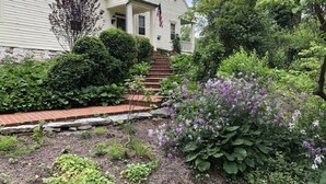 A house with a front porch, a flag, and a garden with various plants and flowers. - Charmingly renovated historic Canal House on C&O along Potomac close to Antietam (Sharpsburg)