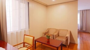 A room with a wooden floor, a beige sofa, a wooden table with a vase, and a chair. - Greentree Alliance Shanghai Railway Station Qiujiang Road Hotel (Shanghai)