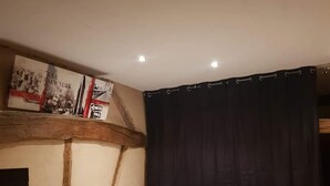 A bedroom with a bed, a nightstand, a lamp, a dark curtain, and a wall with exposed wooden beams and a framed picture. - Bienvenue à l'escale (Gigny-sur-Saône)