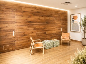 Ein Zimmer mit Holzboden, zwei Holzstühle, ein kleiner Tisch mit Pflanze und ein gerahmtes Kunstwerk an der Wand.