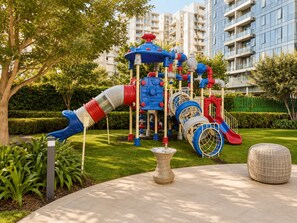 Ein Spielplatz mit Rutschen und Klettergerüsten, umgeben von einem gepflegten Rasen und Bäumen.