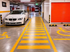 A parking garage with a white car parked in a designated space marked with yellow lines and wheelchair symbols. - Stunning Hi-Rise high speed WiFi , minimalist chic decor, with all the amenities (Ciudad de México)
