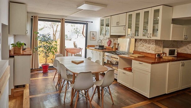 Une cuisine moderne avec des meubles blancs, un coin repas doté d’une table et de chaises en bois, et une vue sur l’extérieur grâce à une porte-fenêtre coulissante.