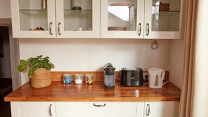 Une cuisine avec des meubles blancs, un plan de travail en bois et divers appareils, notamment une machine à café et un grille-pain.