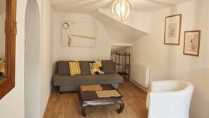 Un salon comprenant un canapé, une table basse, un fauteuil blanc, un luminaire suspendu et un radiateur.