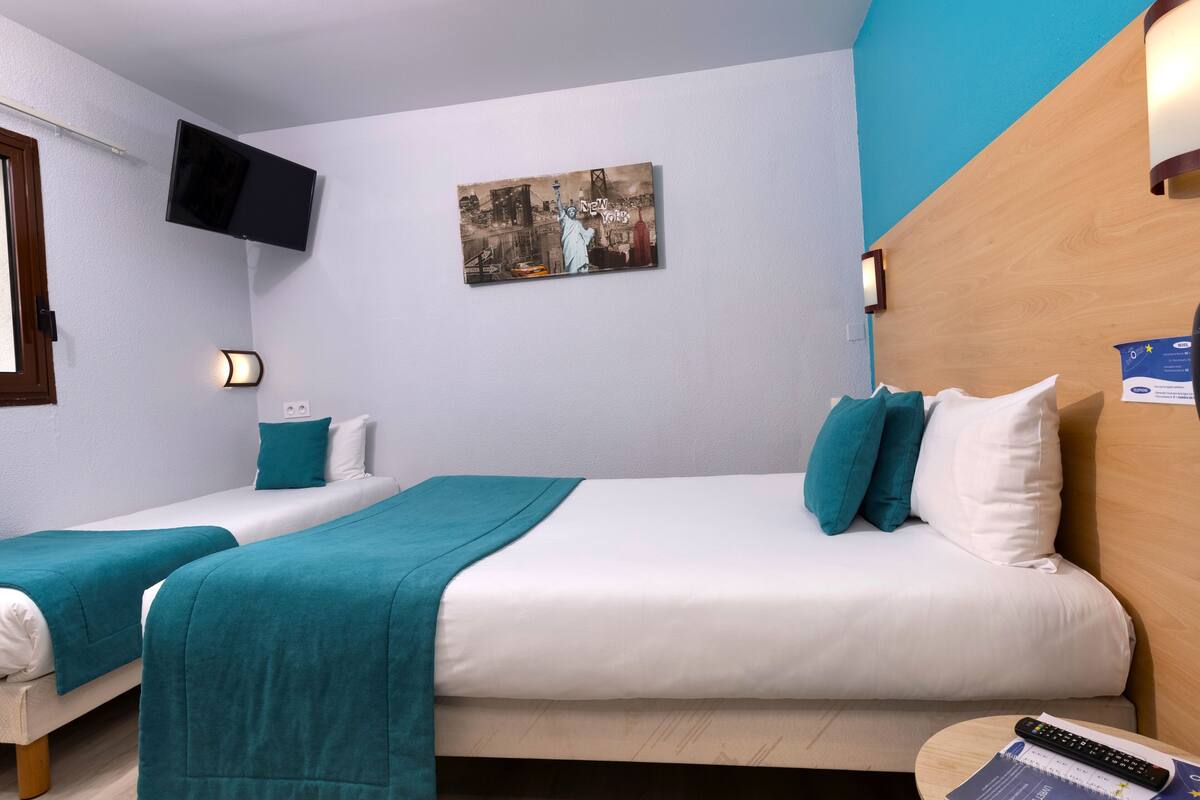 A hotel room with two beds, a flat-screen TV mounted on the wall, a painting, and a wooden headboard.