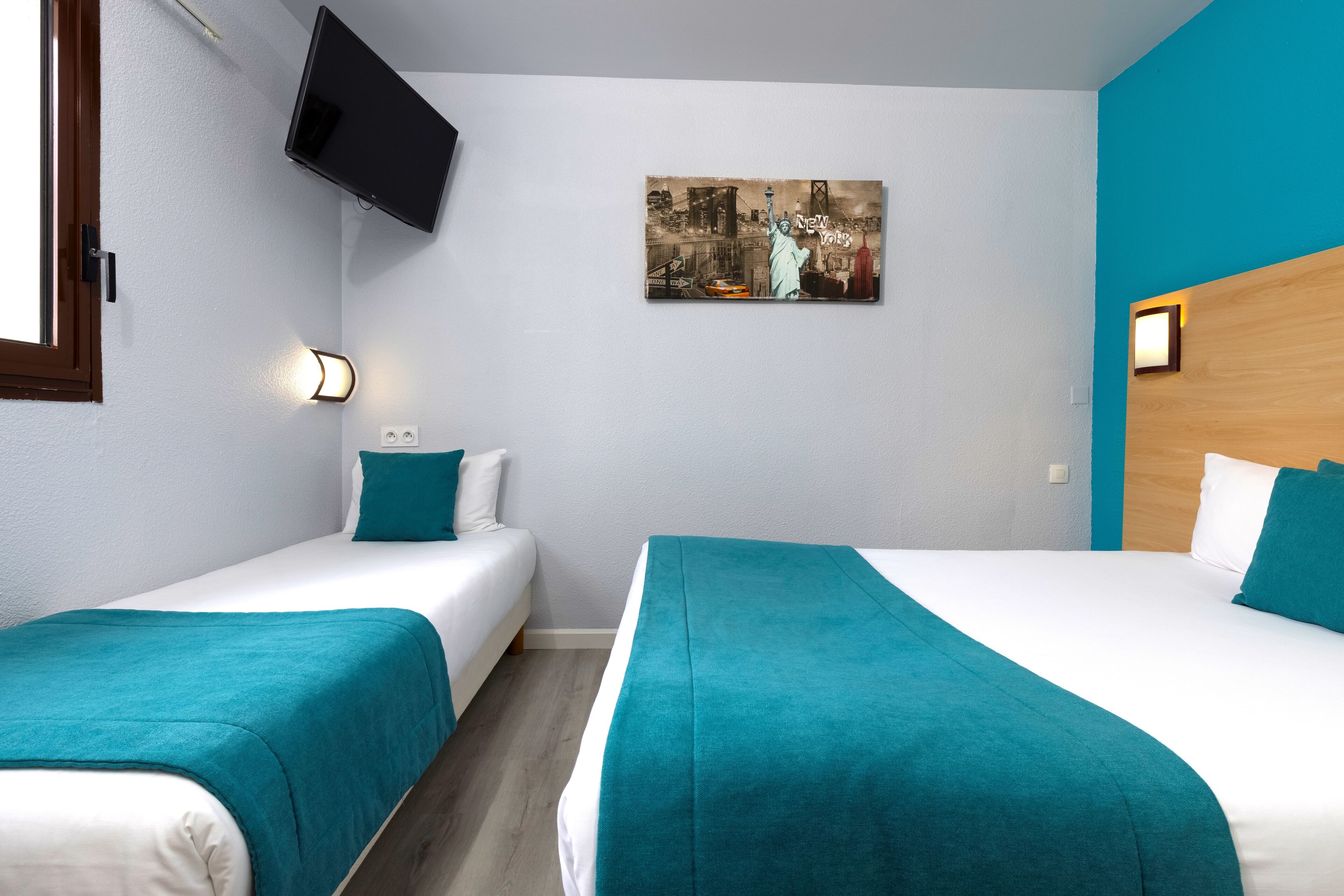Ein Hotelzimmer mit zwei Betten, einem an der Wand montierten Fernseher und einem Bild der Freiheitsstatue.