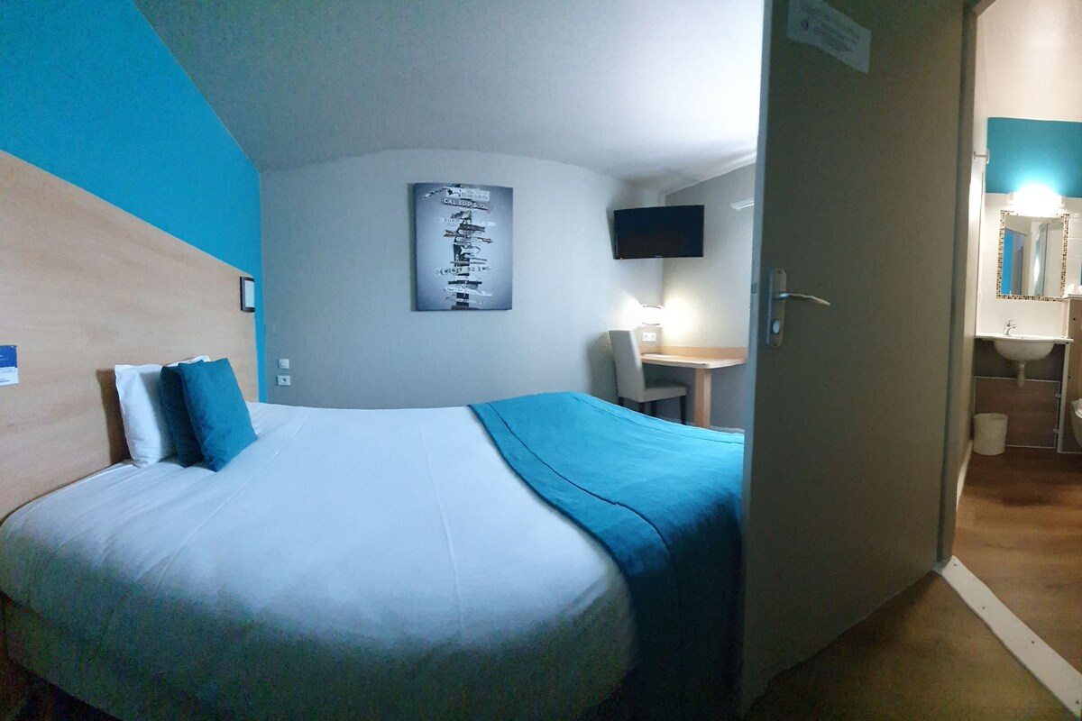 A hotel room with a bed, a desk, a television, and a bathroom visible through an open door.