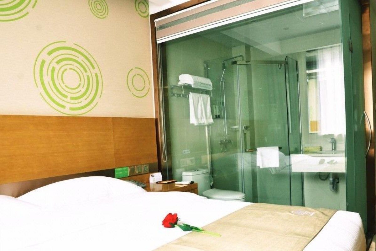 Quarto de hotel com cama, chuveiro em vidro e banheiro com pia e espelho.