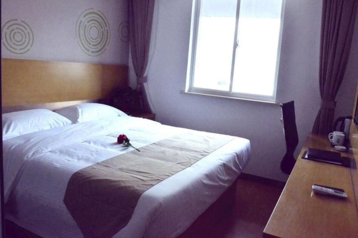 Quarto de hotel com cama, escrivaninha, cadeira, janela e parede com desenhos circulares.