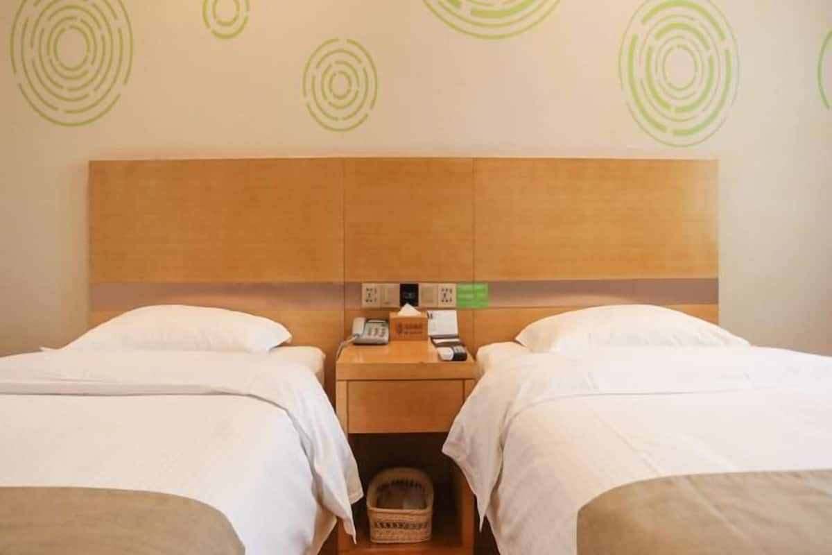 A hotel room with two beds, a wooden headboard, a bedside table with a phone and a lamp, and a wall with circular patterns.