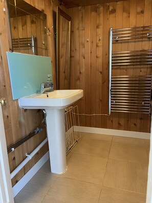 Une salle de bain avec des murs en bois, un lavabo blanc, un miroir, un porte-serviettes et un espace douche.