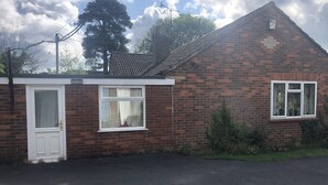 A small brick house with a white door, a window with curtains, and a small garden area. - 2bed Room Small Annex Furnished in High Wycombe (High Wycombe)