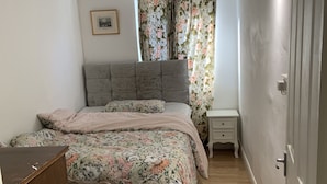 A bedroom with a bed, a nightstand, a dresser, and a window with floral curtains. - 2bed Room Small Annex Furnished in High Wycombe (High Wycombe)