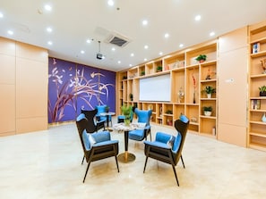 A modern conference room with a round table, blue chairs, a projector screen, and a wall with a floral mural.