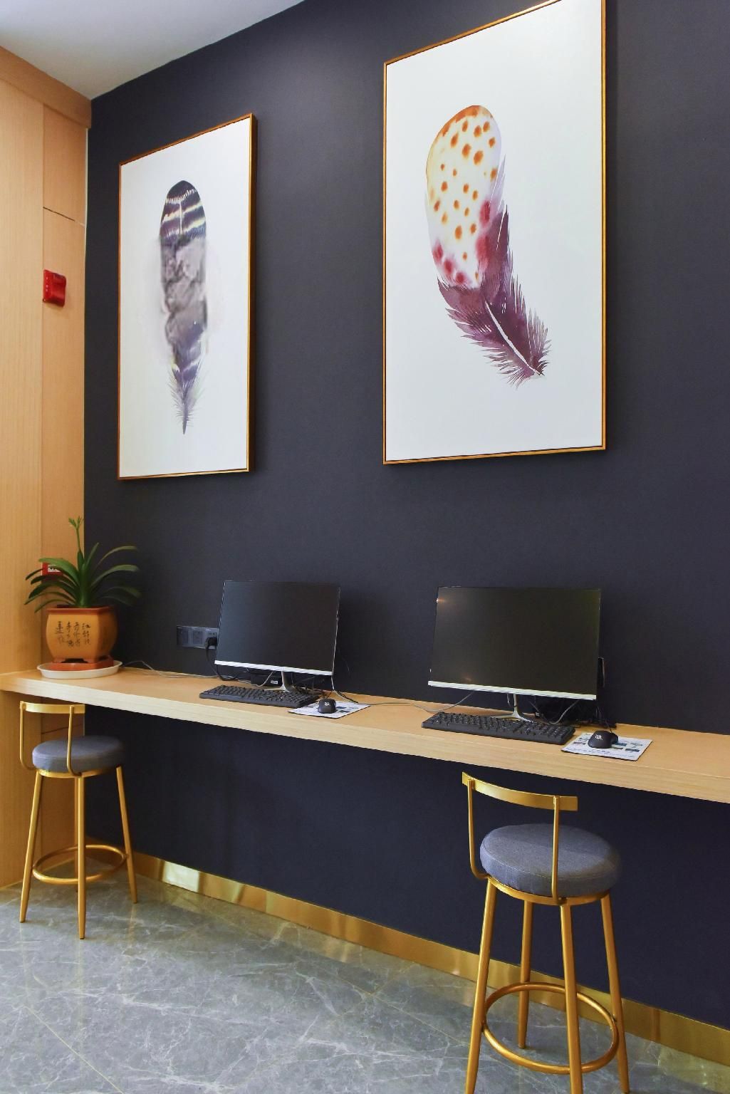 A reception desk with two computer monitors, a potted plant, and two bar stools.