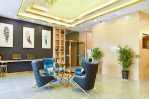 A modern lobby with a reception desk, two blue armchairs, a coffee table, and a decorative ceiling.