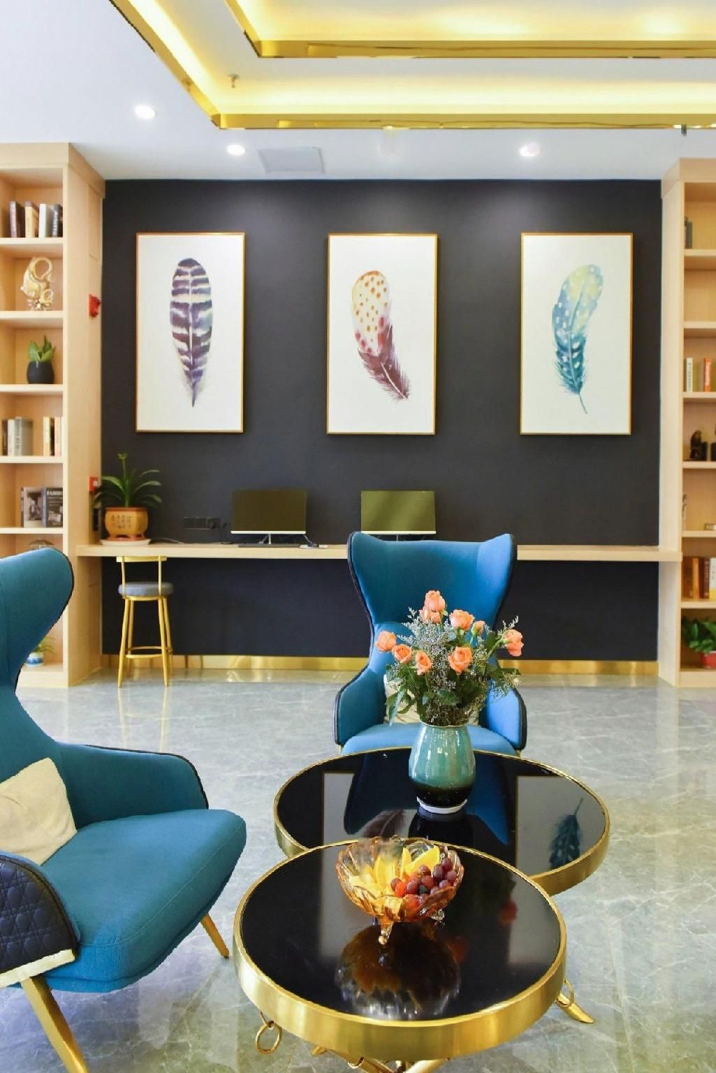 Un lobby moderno con una recepción, un sillón azul, una mesa redonda con un florero y tres obras de arte con plumas en la pared.