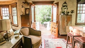A room with a wooden chair, a table with a lamp, and a view of an outdoor garden through an open doorway. - Historic Luxury Condo with POOL & modern amenities in Wildwood Crest, NJ   (Wildwood Crest)