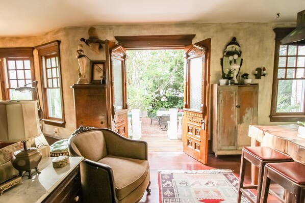 A room with a wooden chair, a table with a lamp, a cabinet, and a view through an open doorway to an outdoor area.