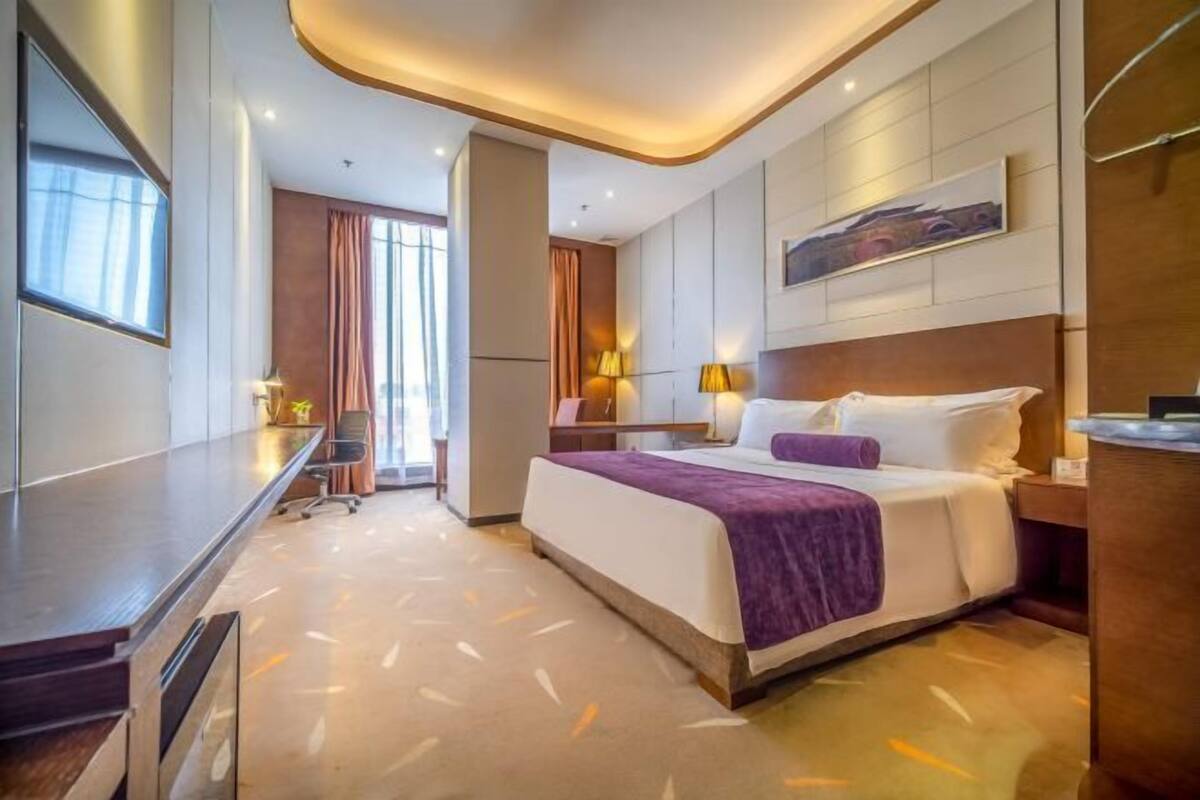A modern hotel room with a large bed, a desk, and a view of the city.