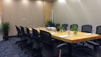 A conference room with a long table, black chairs, potted plants, and water bottles.
