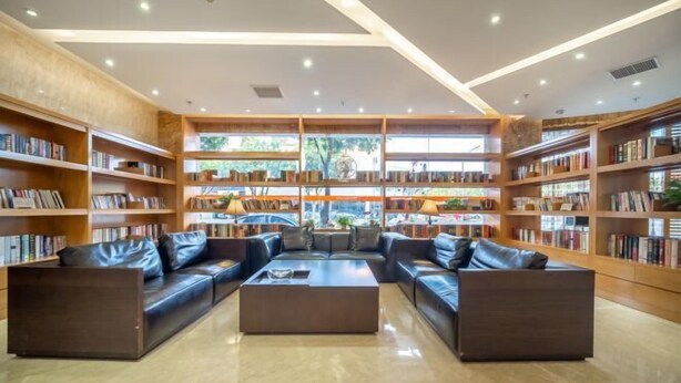 Une bibliothèque moderne, dotée de canapés en cuir, d’étagères en bois et d’une grande fenêtre laissant entrer la lumière naturelle.