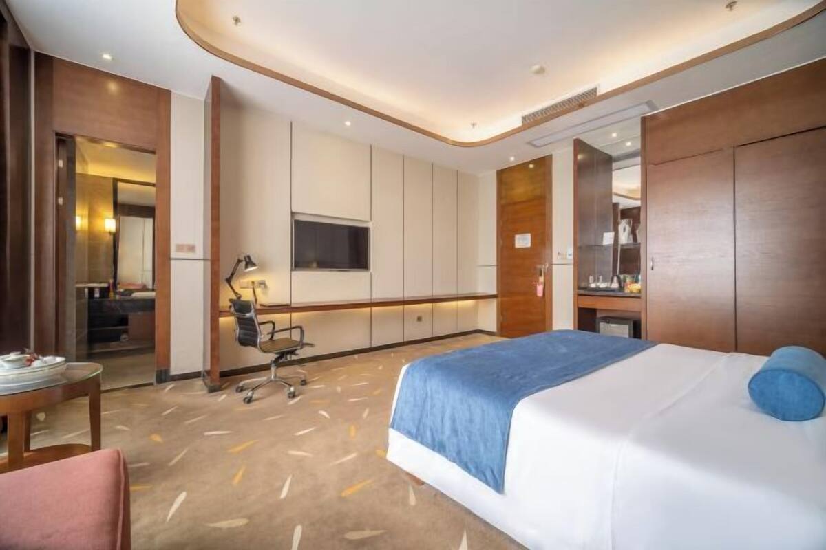 A hotel room with a bed, desk, chair, and a television.