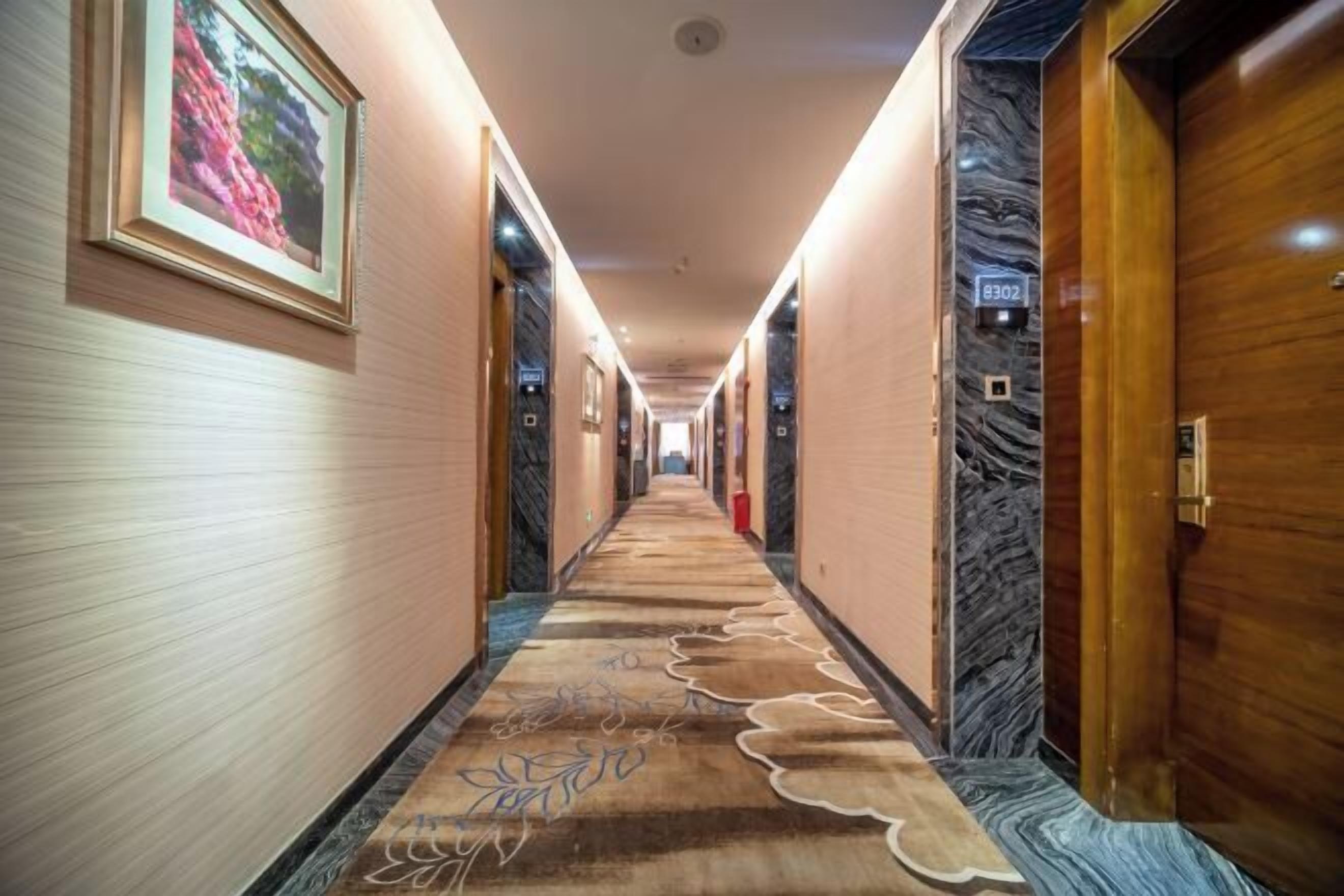 A hotel hallway with a carpeted floor, framed pictures on the walls, and a door with a number sign.