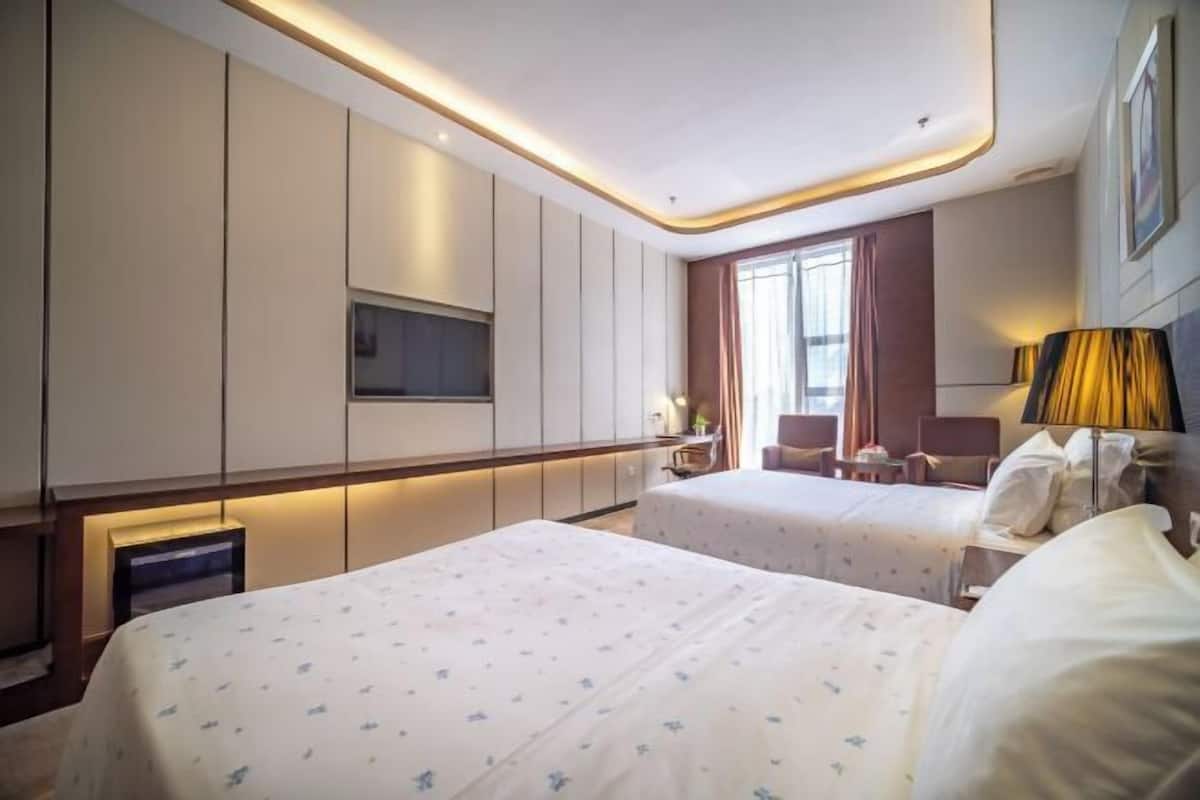 A hotel room with two beds, a TV, a desk, and a window with curtains.
