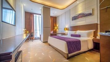 A modern hotel room with a large bed, a desk, and a view of the cityscape.