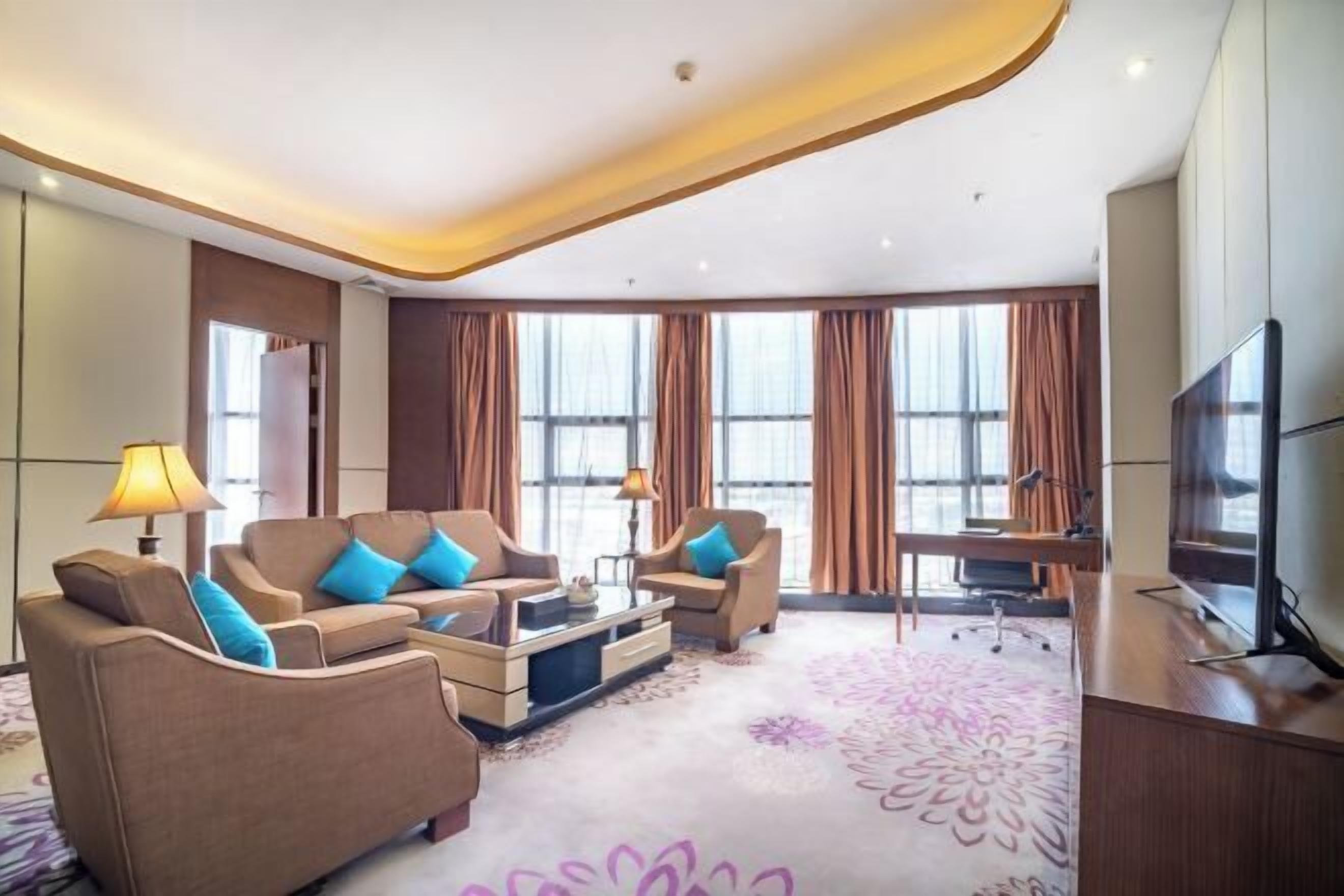 A modern hotel room with a sofa set, a coffee table, a TV, and a desk.