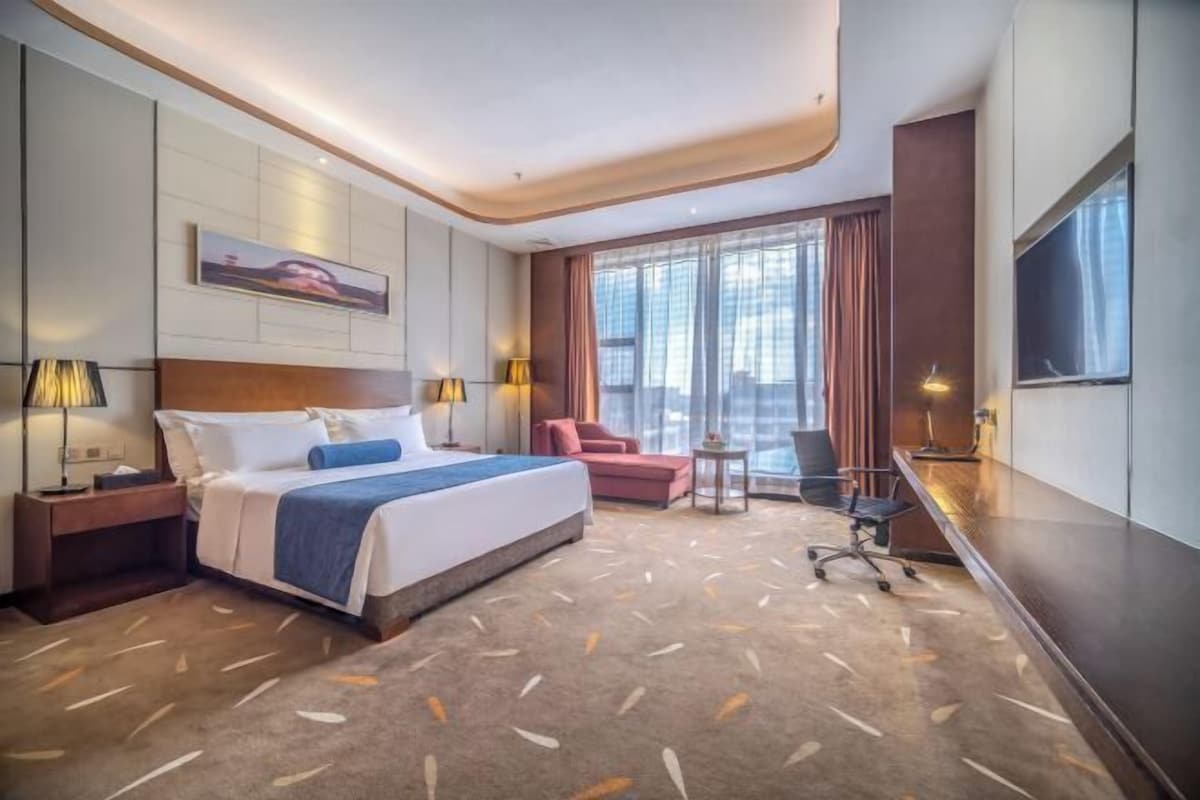 A hotel room with a large bed, a desk, a chair, and a TV.