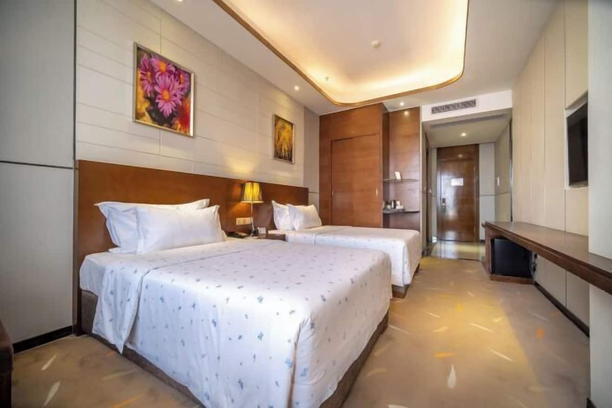 A hotel room with two beds, a wooden headboard, a painting, a desk, and a mirror.