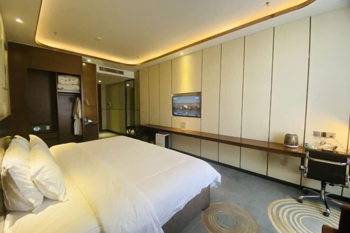 A hotel room with a large bed, a desk with a chair, a television mounted on the wall, and a wardrobe.