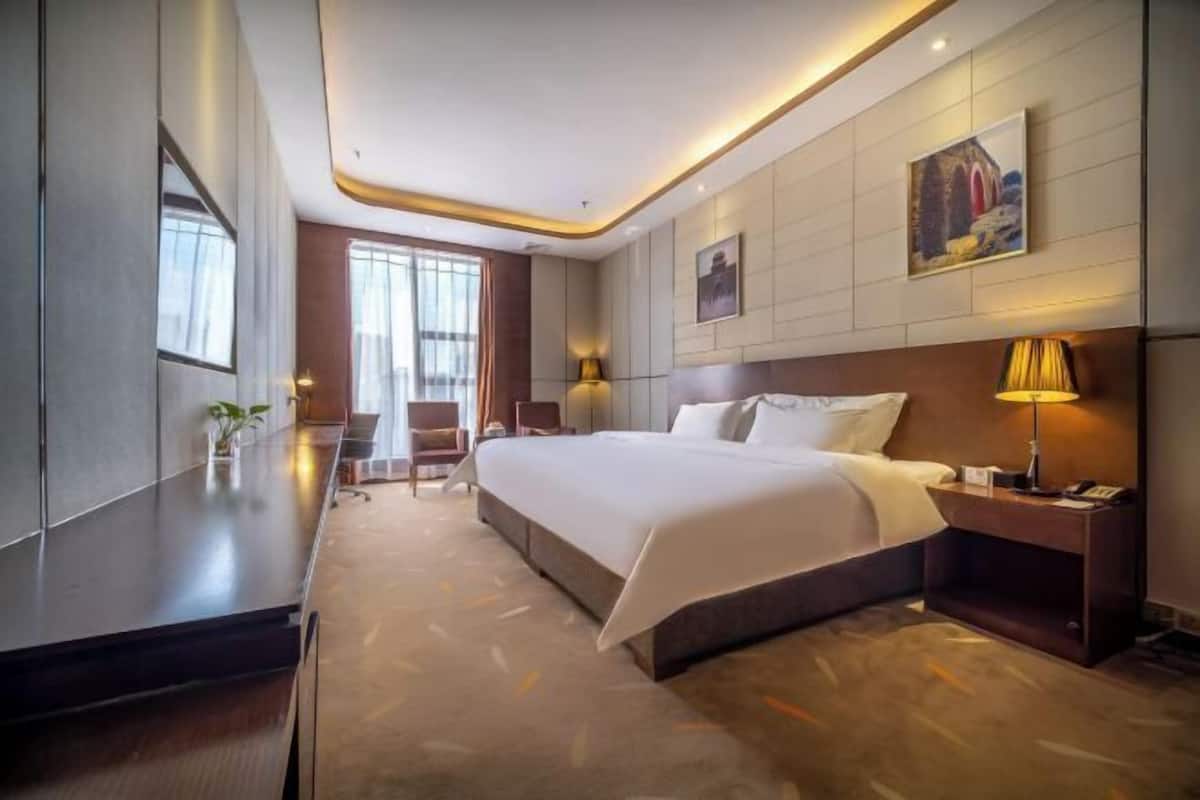 A modern hotel room with a large bed, bedside tables, a desk, and a chair.