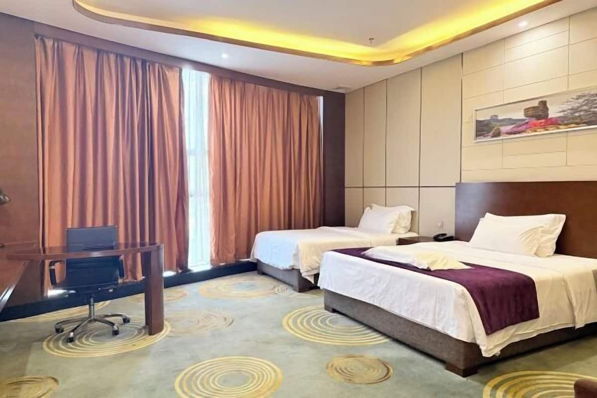 A hotel room with two beds, a desk, and a large window with curtains.