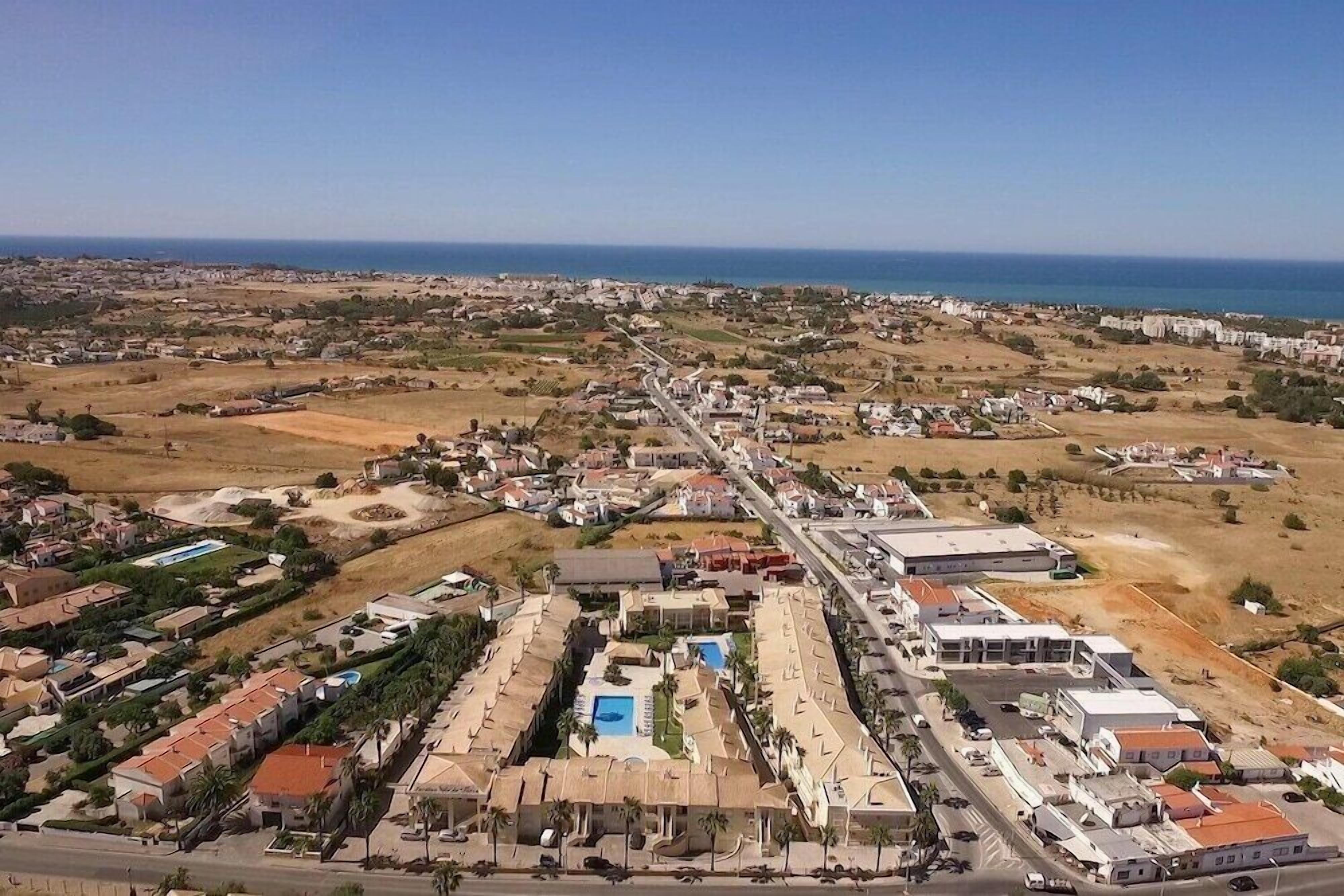 An aerial view of a coastal resort with a central pool, multiple buildings, and a clear view of the ocean.