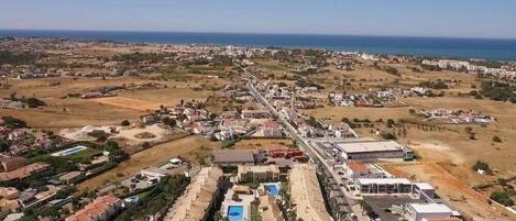 An aerial view of a coastal resort with a central pool, multiple buildings, and a clear view of the ocean.