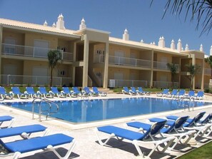 A swimming pool with blue lounge chairs and a building with balconies. - Jardins Vale de Parra (Albufeira)