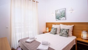 A hotel room with a bed, two nightstands, a lamp, a curtain, and a wall art piece. - Jardins Vale de Parra (Albufeira)