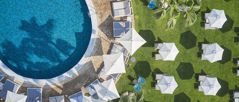 An aerial view of a resort with a swimming pool, sun loungers, and umbrellas.