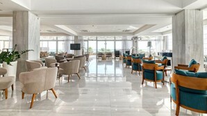 A spacious lobby with marble columns, modern seating, and large windows offering views of the outdoors. - Atlantica Sea Breeze - Adults Only (Paralimni)