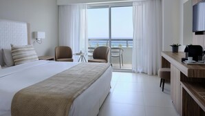 Habitación de hotel moderna con una cama grande, un escritorio con cafetera y vistas al mar desde el balcón.