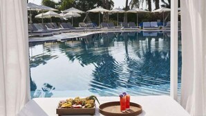 A poolside view with lounge chairs, umbrellas, and a tray with food and drinks. - Atlantica Sea Breeze - Adults Only (Paralimni)